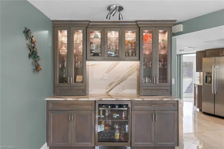 Bar with a bar, wine cooler, backsplash, and stainless steel fridge