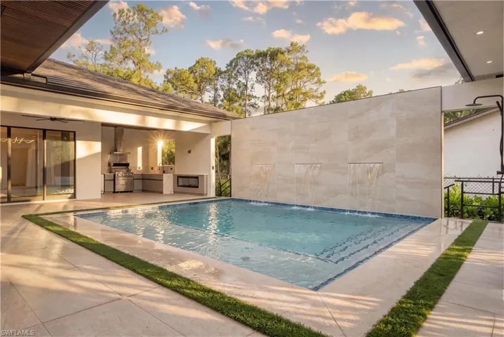 Swimming pool with three cascading water features, expansive patio, outdoor kitchen with built-in grill and range hood, and an outdoor shower