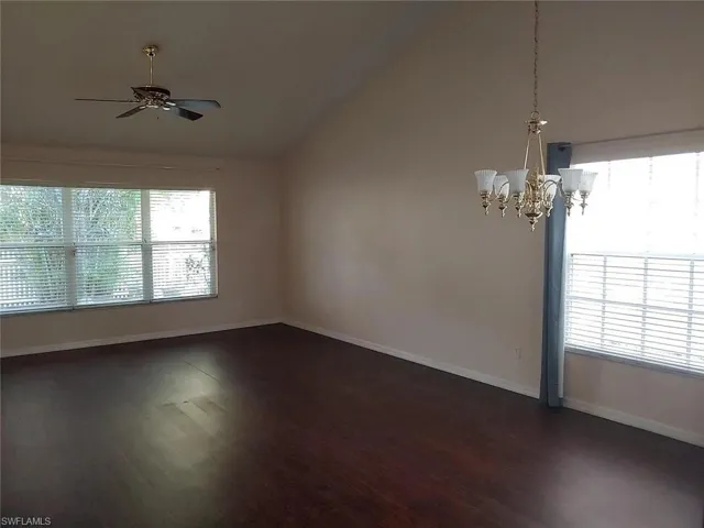 Spare room featuring vaulted ceiling, dark wood-style floors, hanging lights, and ceiling fan