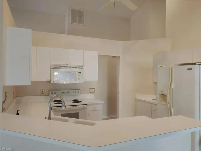 Kitchen with light countertops, white appliances, white cabinets, a peninsula, and a high ceiling