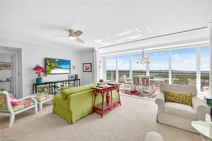 Carpeted living area with a chandelier, ceiling fan, and ornamental molding