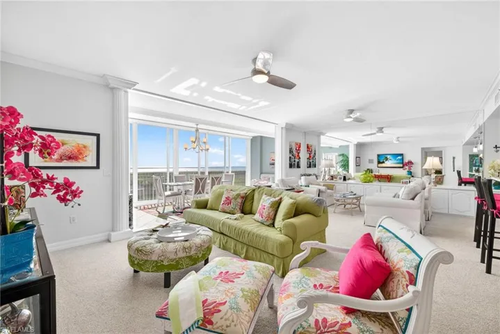 Living room featuring crown molding, ceiling fan, light colored carpet, a chandelier, and ornate columns