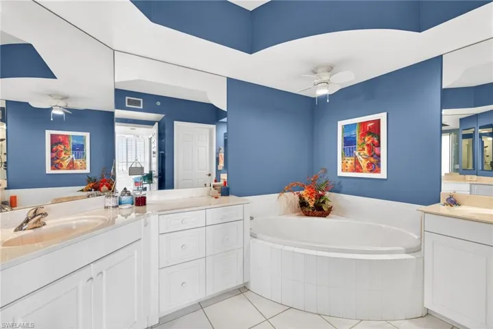 Bathroom featuring a ceiling fan, a garden tub, two vanities, and light tile patterned floors
