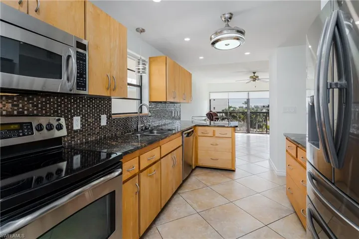 Kitchen with kitchen peninsula, stainless steel appliances, ceiling fan, sink, and light tile patterned flooring