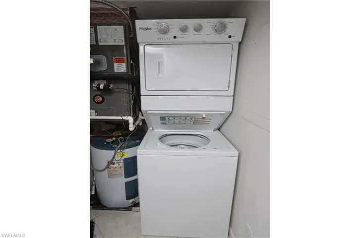 Washroom featuring stacked washer / dryer, light tile flooring, and water heater