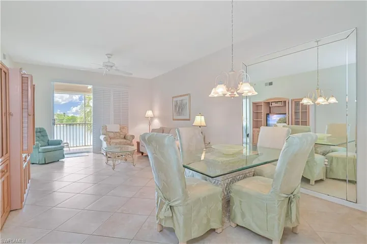 Open concept living and dining area featuring tile flooring, a glass-top dining table, a full-wall mirror, and a sliding glass door leading to a balcony with water scenery