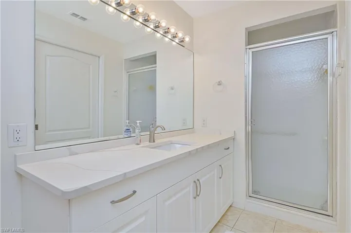 Bright bathroom featuring a spacious vanity with a light-toned countertop, integrated sink, and an extensive mirror with overhead lighting