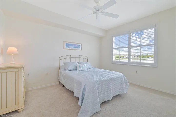 Interior room featuring wall-to-wall carpeting, a large window with white plantation shutters, a ceiling fan, and light-toned walls