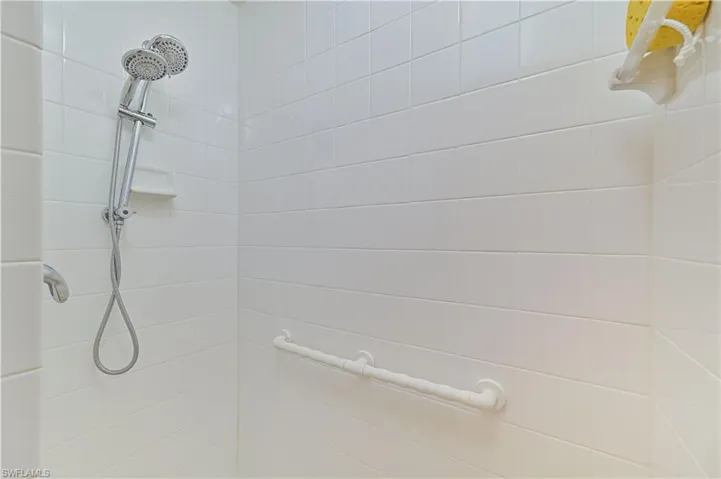 Tiled shower stall featuring a chrome dual showerhead, built-in soap dish, and a white grab bar