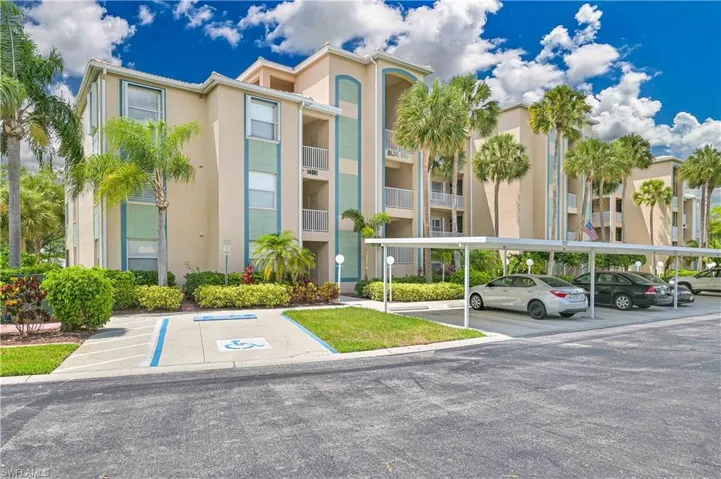 Multi-story building featuring stucco exterior, multiple balconies with white railings, and lush landscaping including mature palm trees