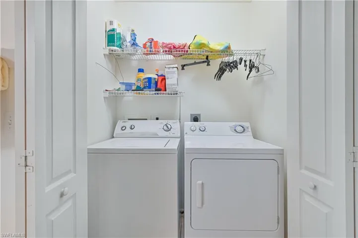 Dedicated laundry area featuring a white washing machine and dryer, two wire shelving units, and bi-fold closet doors