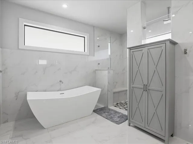 Bathroom featuring a freestanding bath, a marble finish shower, stone wall, light marble finish floors, and tile walls