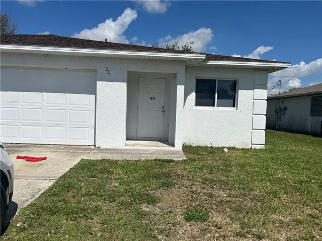 View of front of home with stucco siding, a front yard, concrete driveway, and a garage