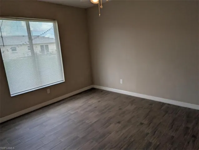 Unfurnished room with dark wood-style flooring, baseboards, and ceiling fan