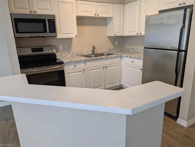 Kitchen with appliances with stainless steel finishes, a sink, dark wood finished floors, white cabinets, and light countertops