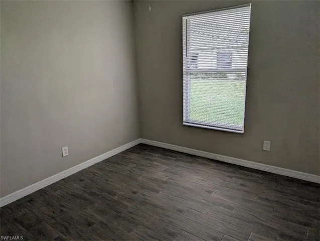 Unfurnished room with dark wood-type flooring and baseboards