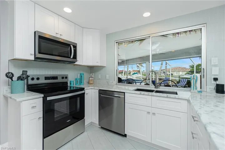 Kitchen featuring sink, light stone counters, stainless steel appliances, white cabinets, and decorative backsplash