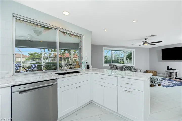 Kitchen with dishwasher, light stone counters, white cabinets, sink, and kitchen peninsula