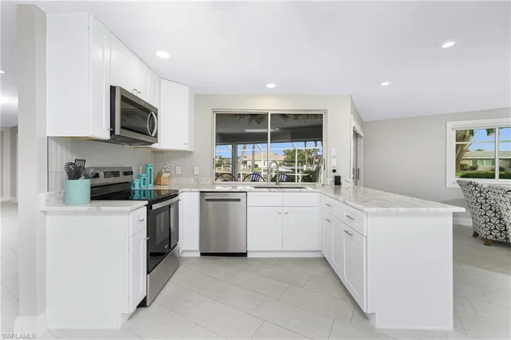 Kitchen with appliances with stainless steel finishes, sink, light stone counters, white cabinetry, and decorative backsplash
