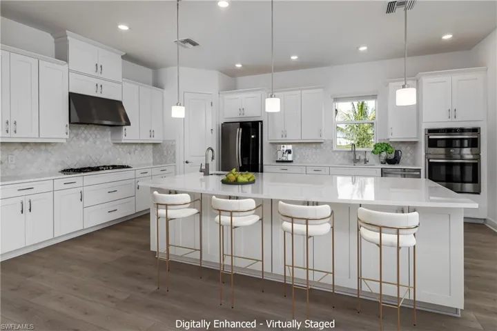 Kitchen with hardwood / wood-style floors, tasteful backsplash, an island with sink, stainless steel appliances, and white cabinetry