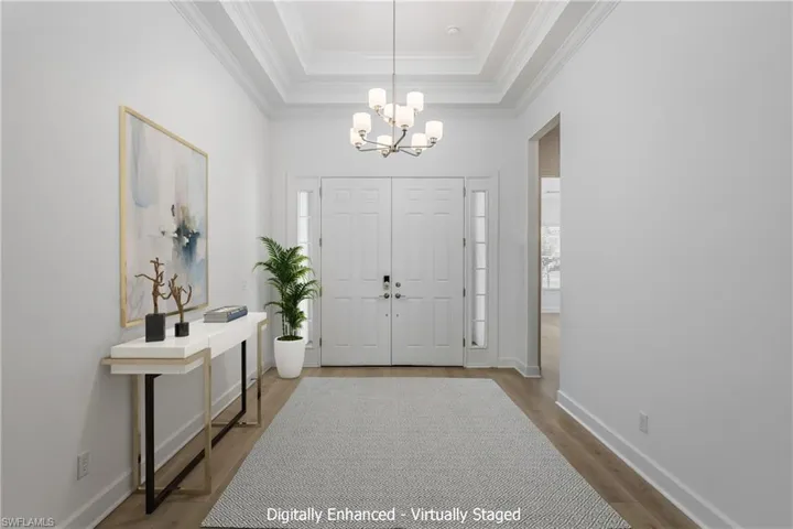 Foyer with crown molding, an inviting chandelier, hardwood / wood-style floors, and a raised ceiling