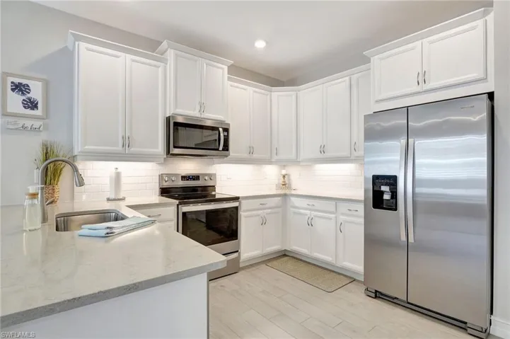 Kitchen featuring white cabinets, appliances with stainless steel finishes, sink, and light stone countertops