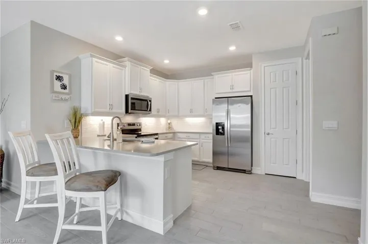 Kitchen featuring appliances with stainless steel finishes, white cabinetry, a breakfast bar area, and tasteful backsplash