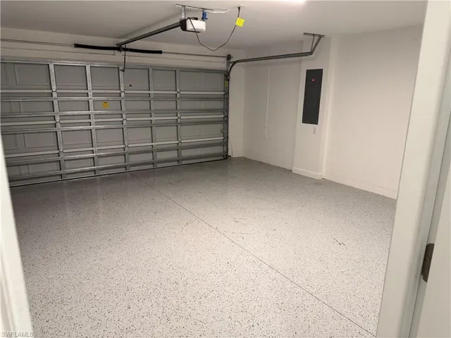 Spacious garage featuring a speckled epoxy floor, white painted walls, an automatic garage door opener, and a wall-mounted electrical panel