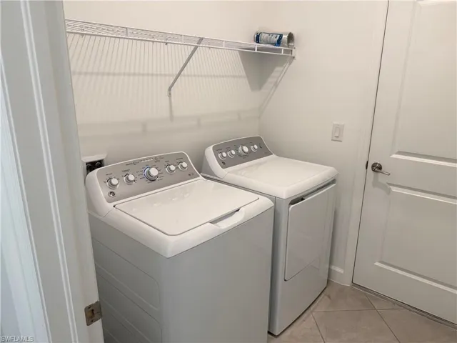 Dedicated laundry area featuring a washer and dryer, tile flooring, and a wire storage shelf