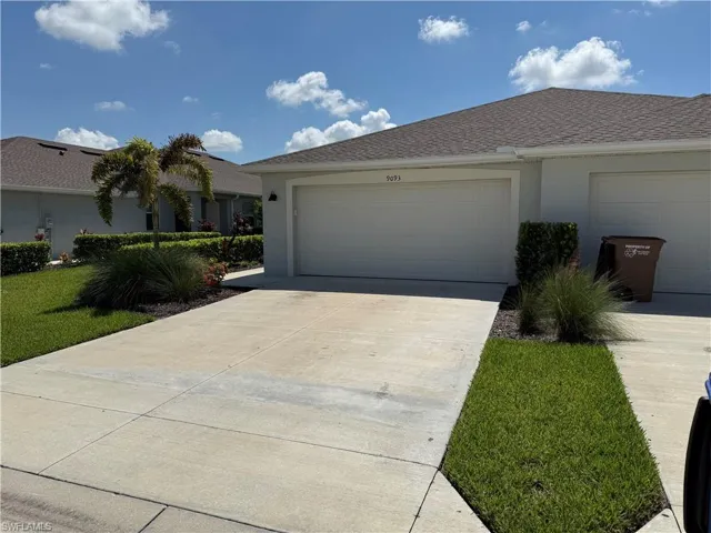 Concrete driveway with a two-car garage, manicured lawn, and established landscaping featuring a palm tree and shrubs