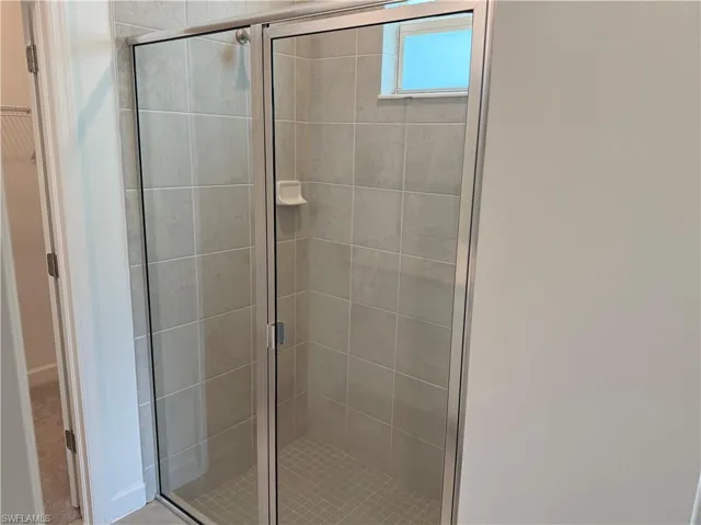 Walk-in shower featuring light-toned tile, a glass enclosure with a silver-tone frame, and a small window for natural light