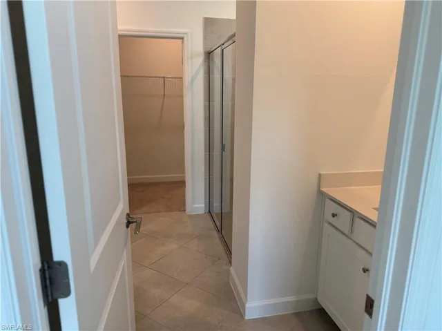 Bathroom featuring a glass-enclosed shower, single vanity with light-colored countertop, white cabinetry with silver hardware, and diagonally-laid floor tiles