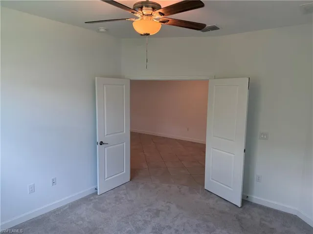 Interior space featuring a ceiling fan with light fixture, light gray carpeting, and white baseboards