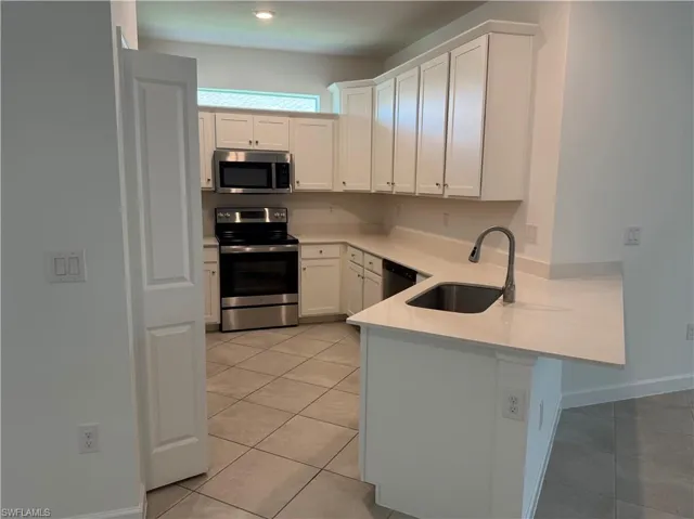 Modern kitchen featuring white cabinetry, light-toned countertops, stainless steel appliances, and a stainless steel sink with a gooseneck faucet