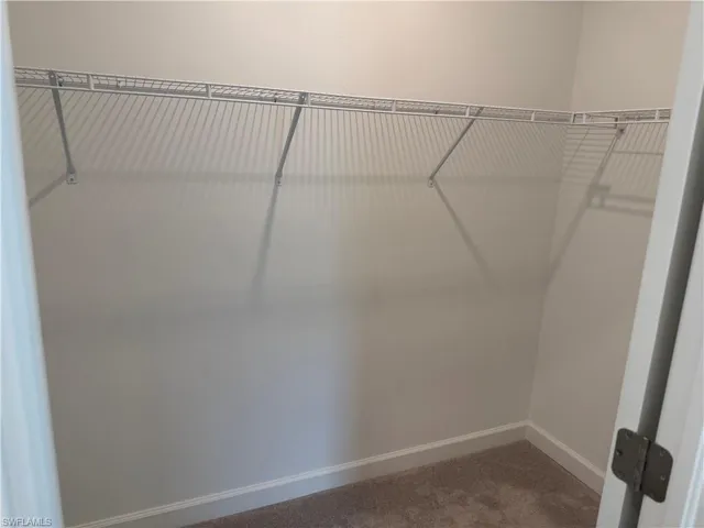Walk-in closet featuring light grey walls, white wire shelving, white baseboards, and carpet flooring