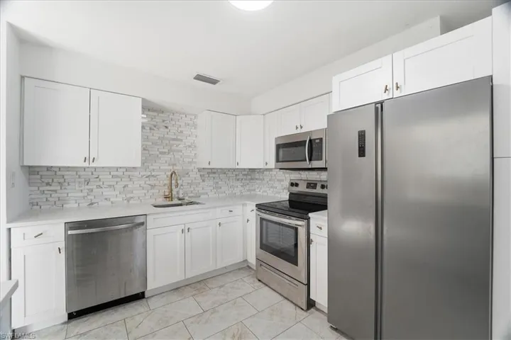 Kitchen with stainless steel appliances, white cabinets, decorative backsplash, and light stone counters