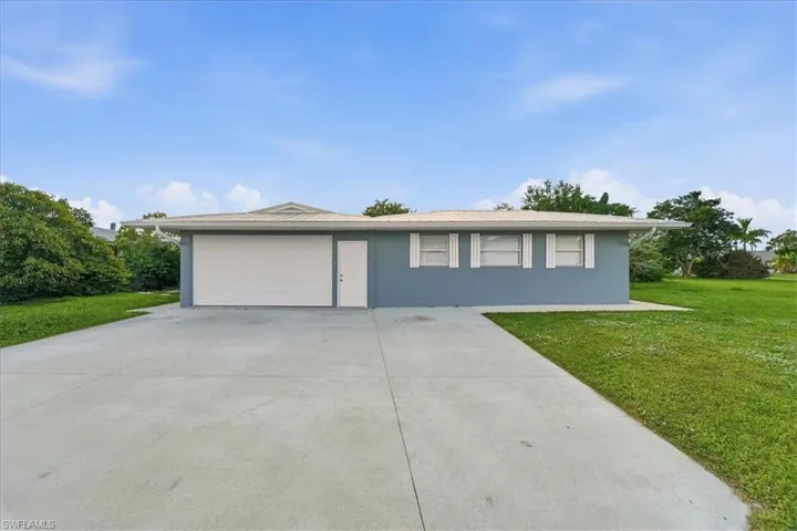 Ranch-style home with a front lawn, driveway, an attached garage, and stucco siding