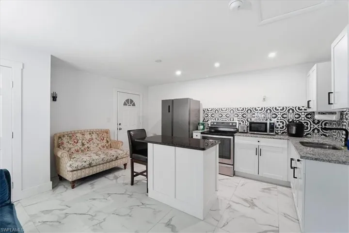 Kitchen with a breakfast bar, dark stone countertops, light marble finish floors, appliances with stainless steel finishes, and white cabinets