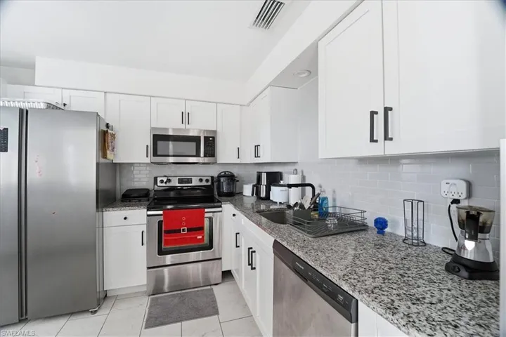 Kitchen featuring appliances with stainless steel finishes, light stone counters, white cabinetry, and tasteful backsplash