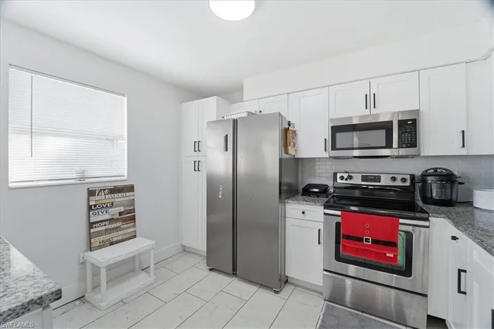 Kitchen featuring stainless steel appliances, white cabinetry, and light stone countertops