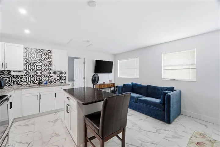 Kitchen featuring dark stone counters, light marble finish floors, white cabinetry, and open floor plan