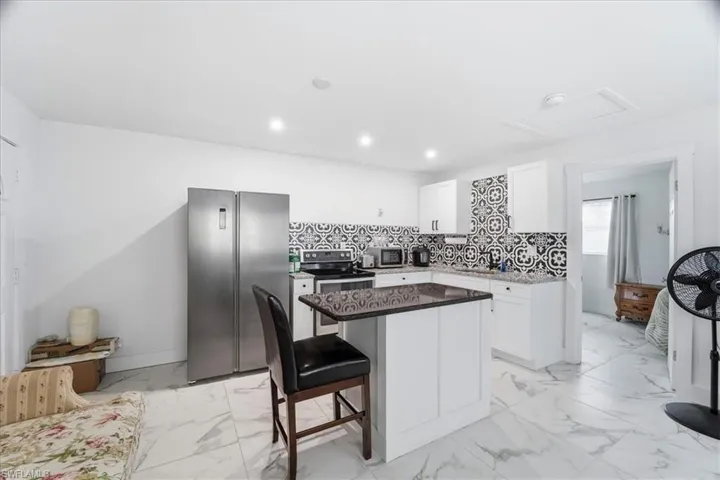Kitchen with appliances with stainless steel finishes, a kitchen bar, a kitchen island, white cabinets, and light marble finish floors