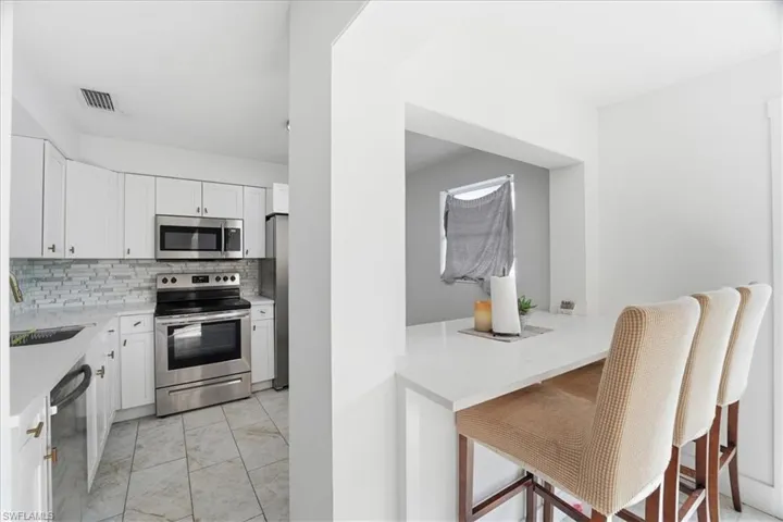 Kitchen with appliances with stainless steel finishes, white cabinets, light stone counters, decorative backsplash, and a kitchen breakfast bar