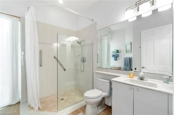 Bathroom with vanity, tiled shower, toilet, and wood finished floors