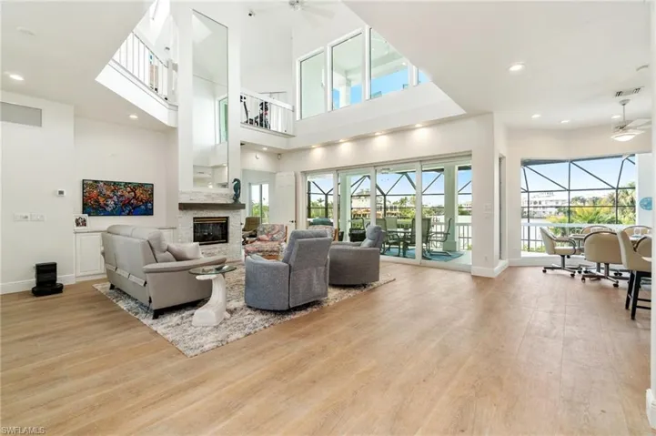 Living room featuring a ceiling fan, a fireplace, wood finished floors, baseboards, and a towering ceiling