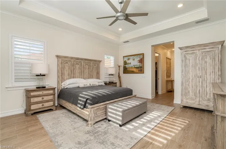 Primary bedroom featuring a raised ceiling, ceiling fan, tiled flooring, and crown molding
