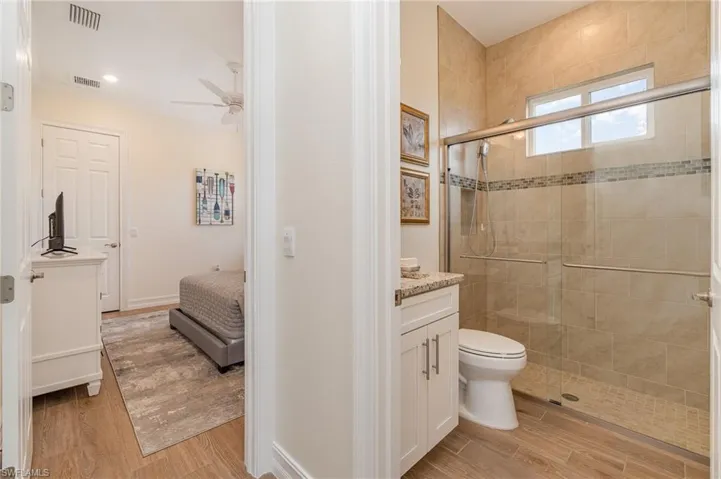 Bathroom featuring vanity, a shower with door, ceiling fan,  tiled flooring, and toilet
