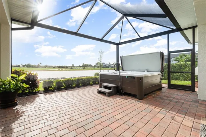 View of patio / terrace featuring a lanai, a water view, golf course view and a hot tub