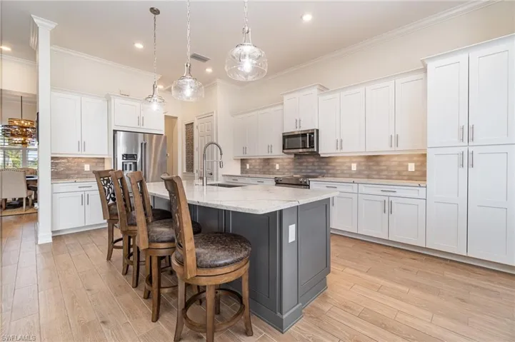 Kitchen with white cabinets, a center island with sink,  decorative light fixtures, and stainless steel appliances