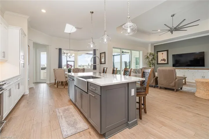Kitchen with light  countertops, a kitchen island with sink, pendant lighting, and white cabinets